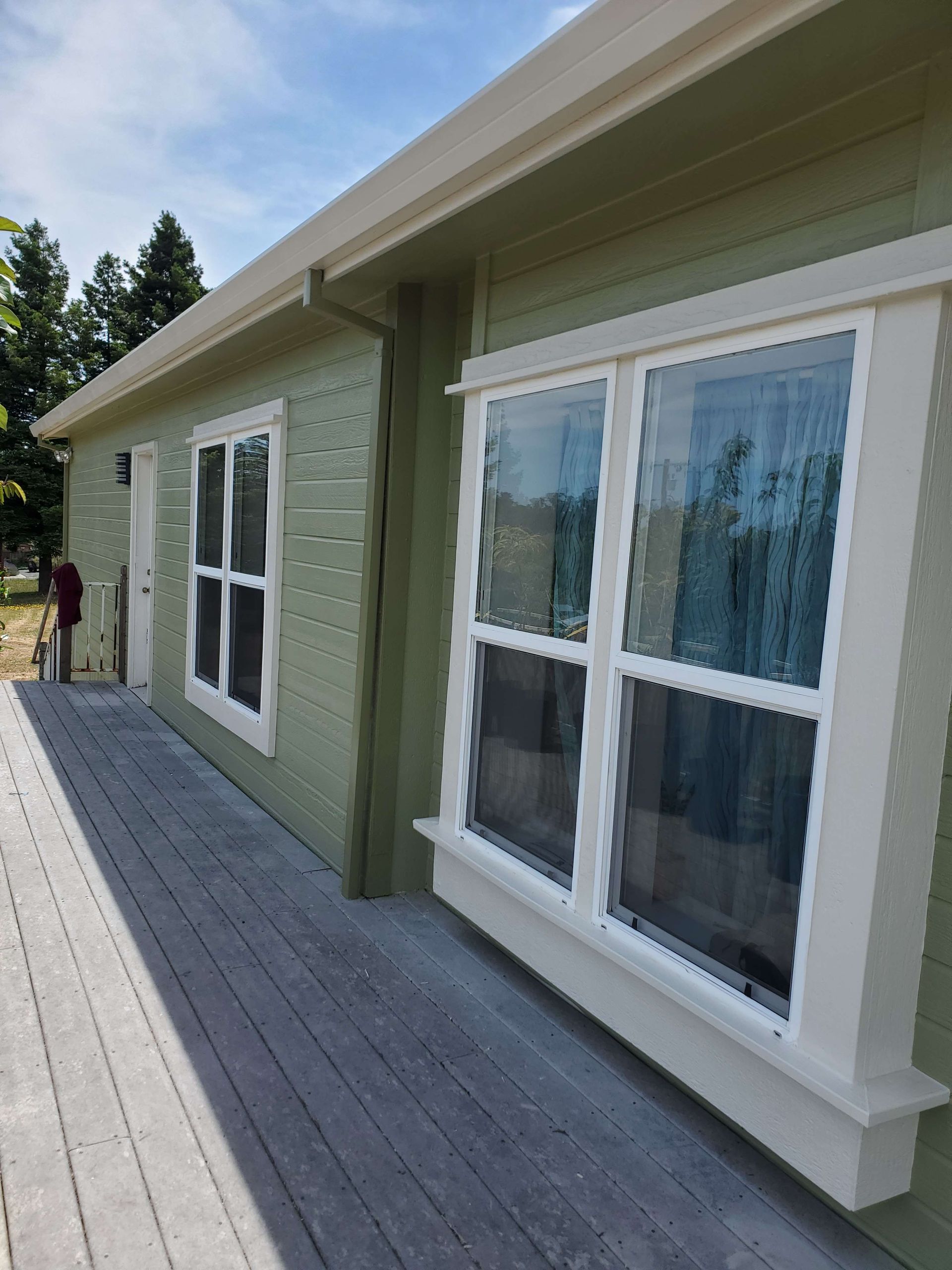 A light green house exterior with a wide wooden porch and white-trimmed windows under a clear blue sky.