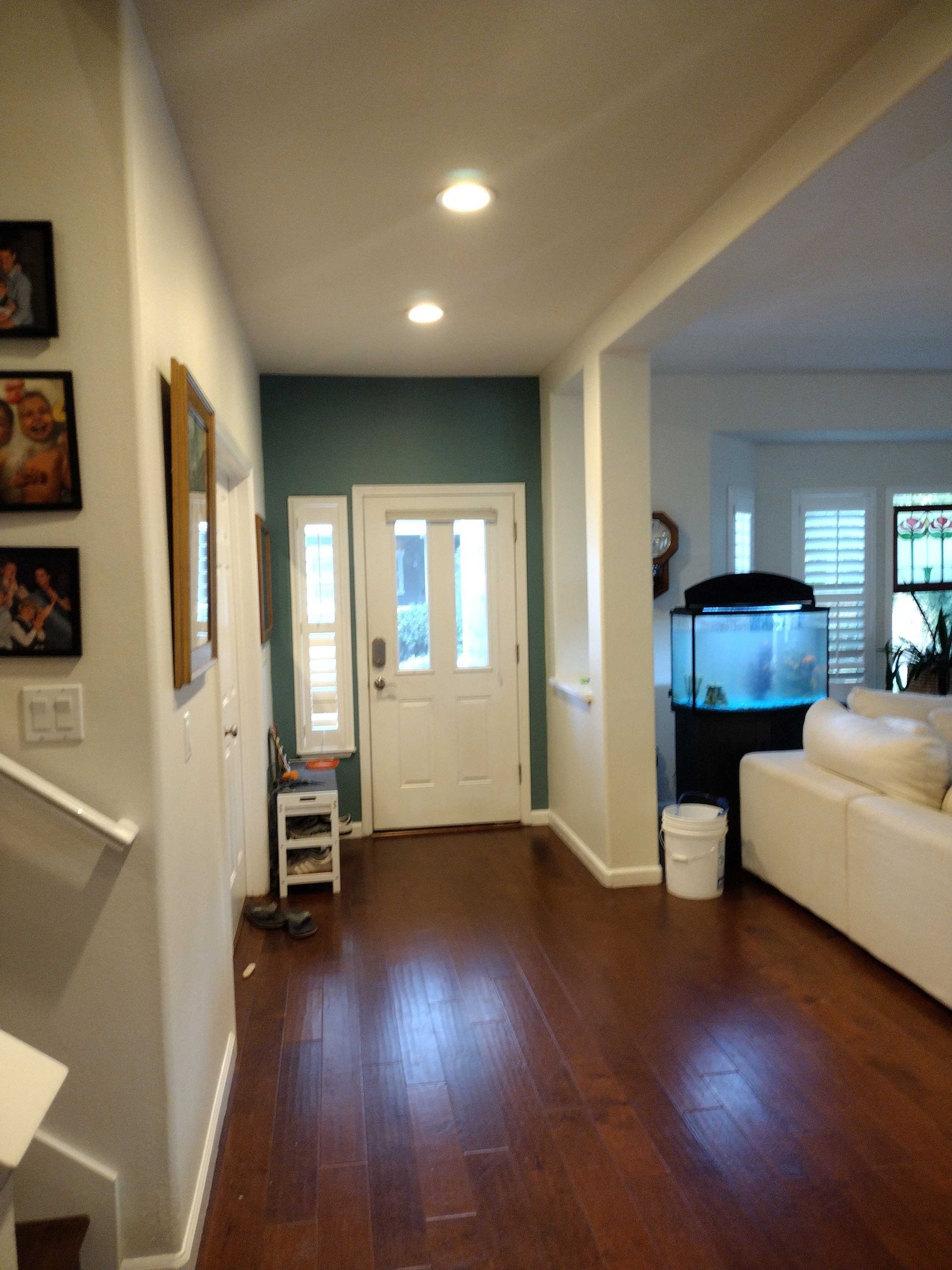 Two people use blue painter's tape to prep a white wall for painting in a room with track lighting.