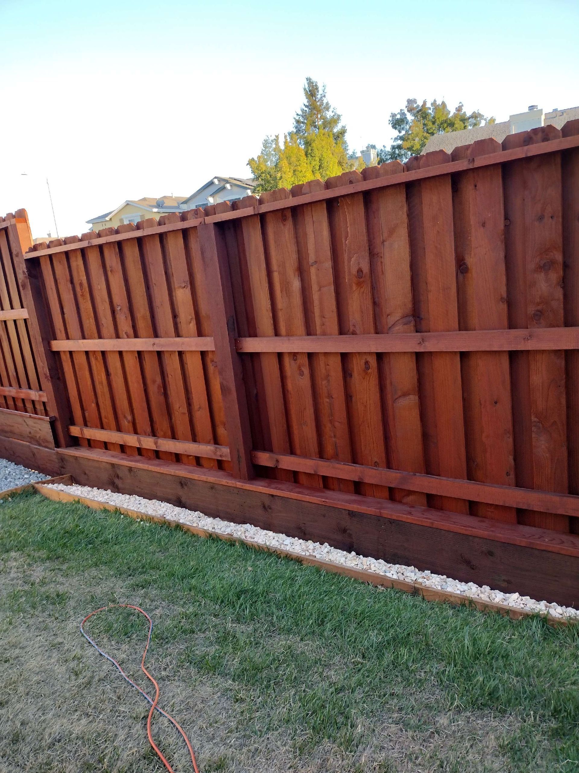 Tilted wooden backyard fence beside a grass lawn under a bright sky