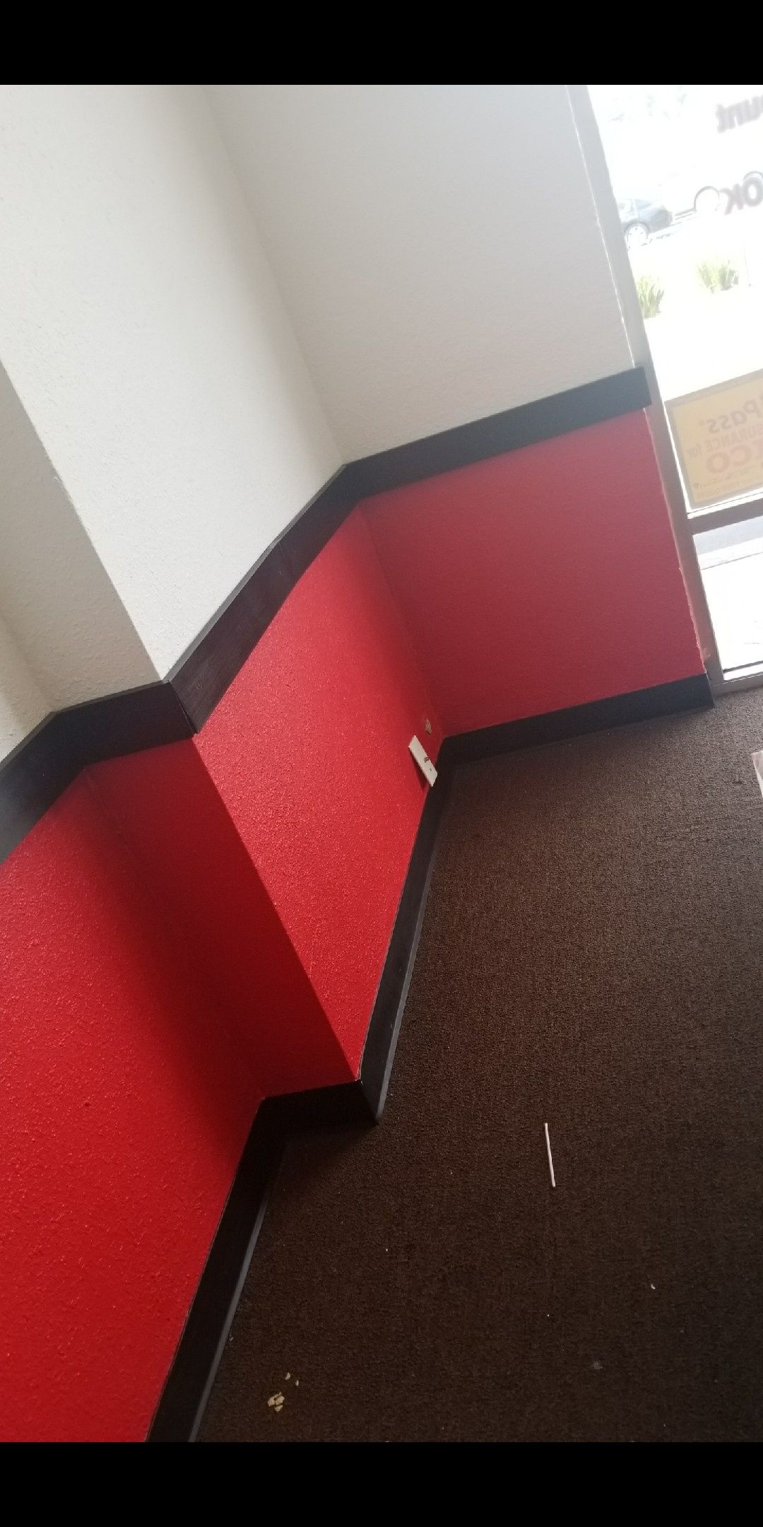 Hallway corner with red lower walls, white upper walls, black trim, and dark carpet near a bright doorway