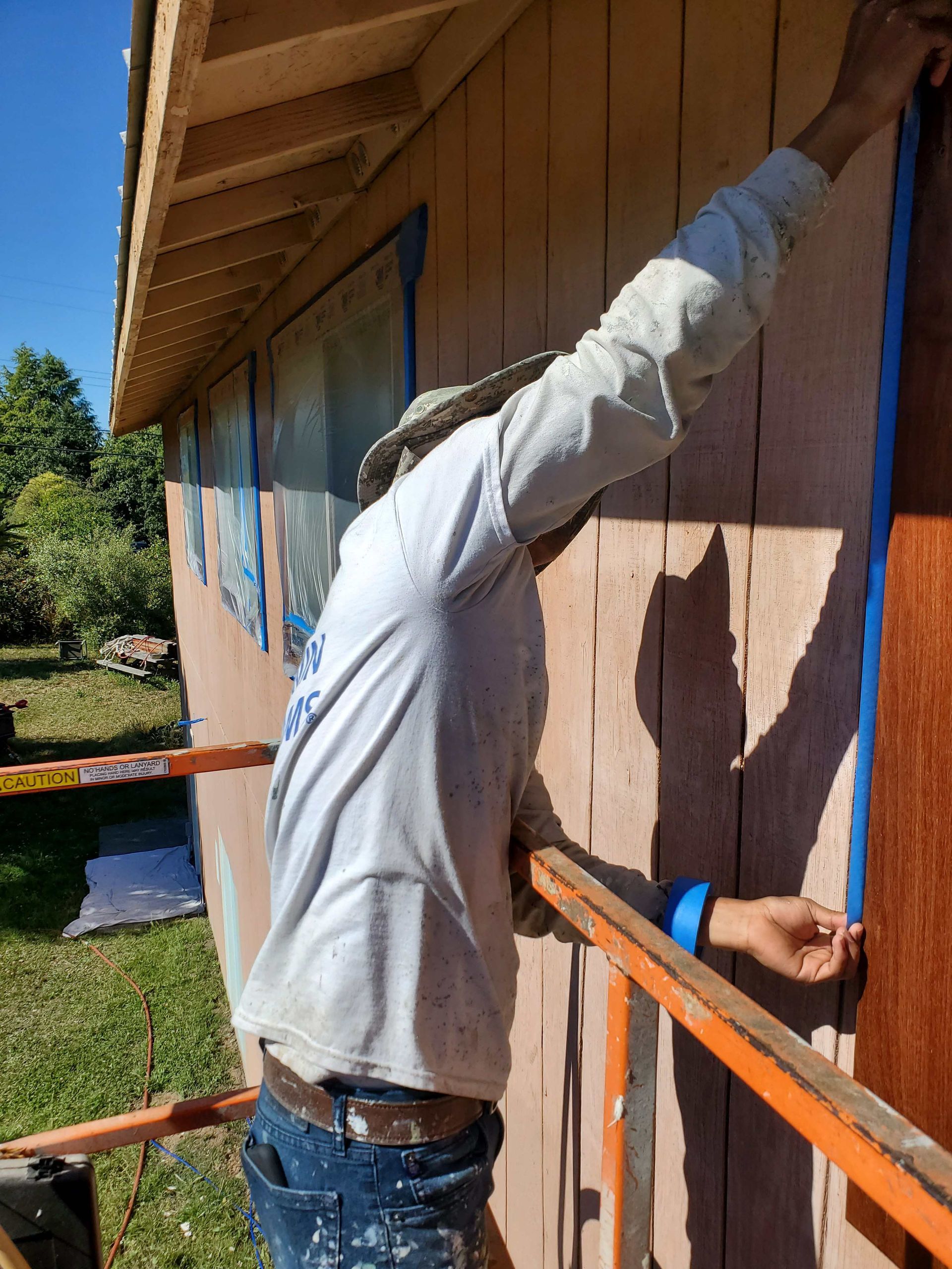 Two people apply blue painter's tape to a wall in preparation for painting, while working together in a room.
