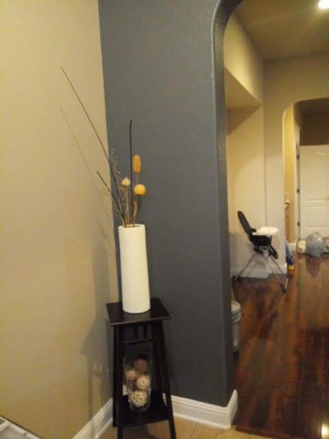 Hallway with gray archway, narrow shelf holding a white vase, and wood floor leading to a distant room