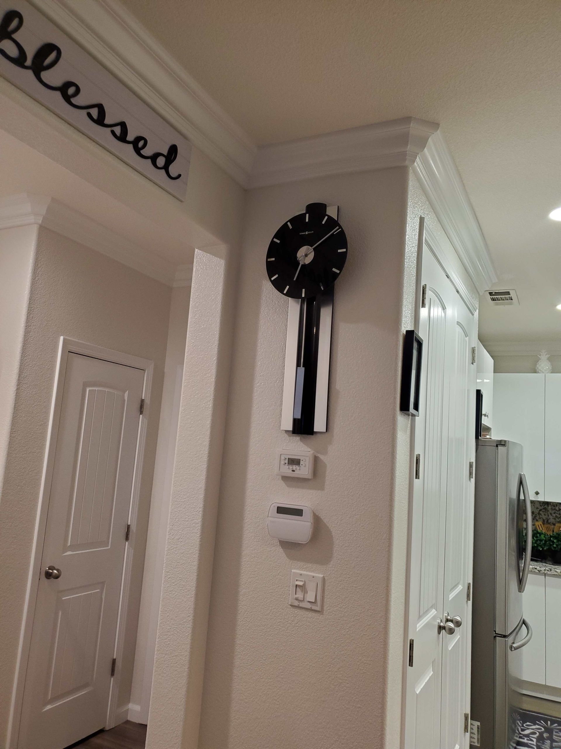 Hallway with wall clock, thermostat, and white doors in a beige home interior