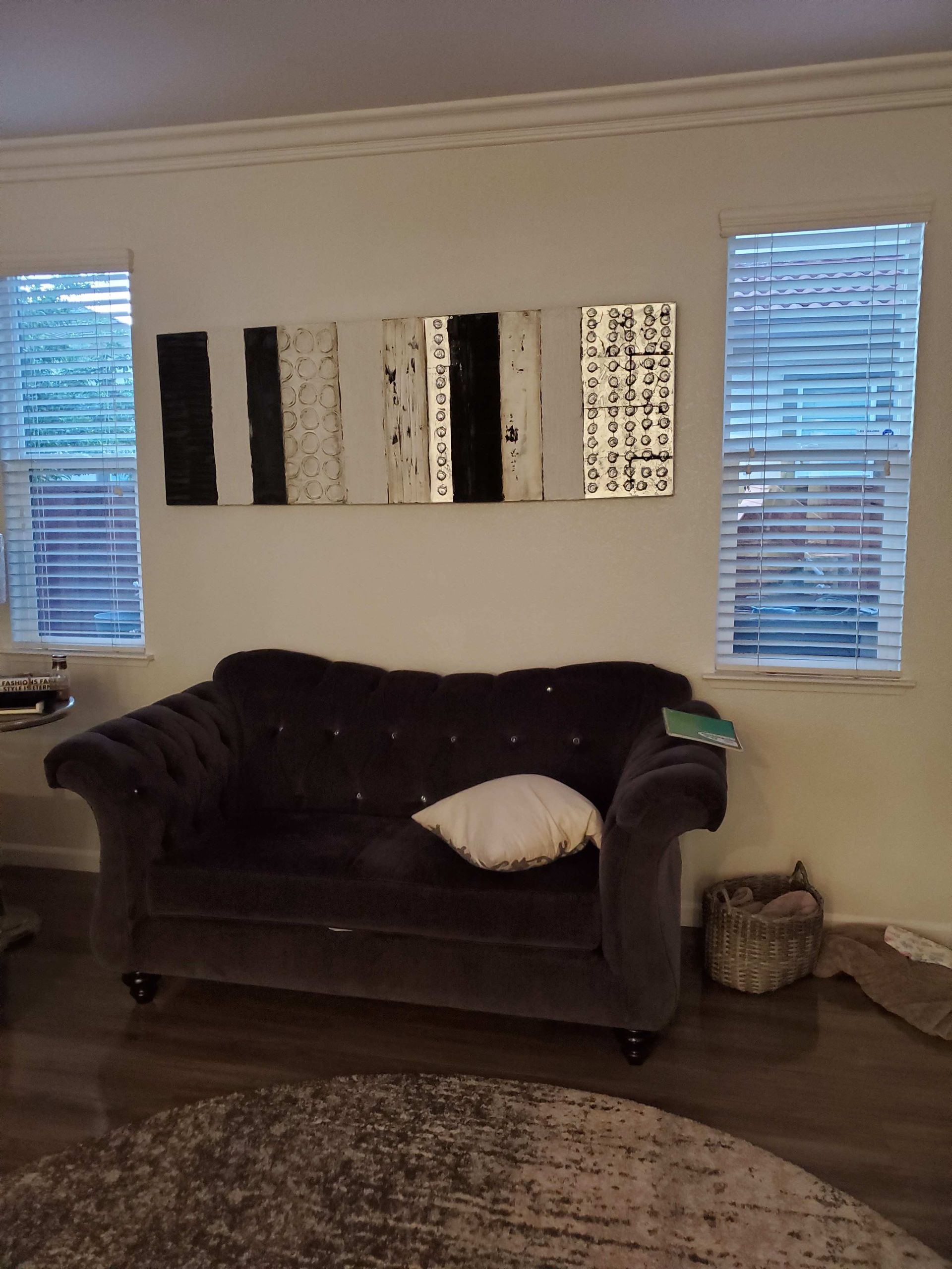 Living room with dark sofa, striped wall art, two windows, rug, and basket on wood floor