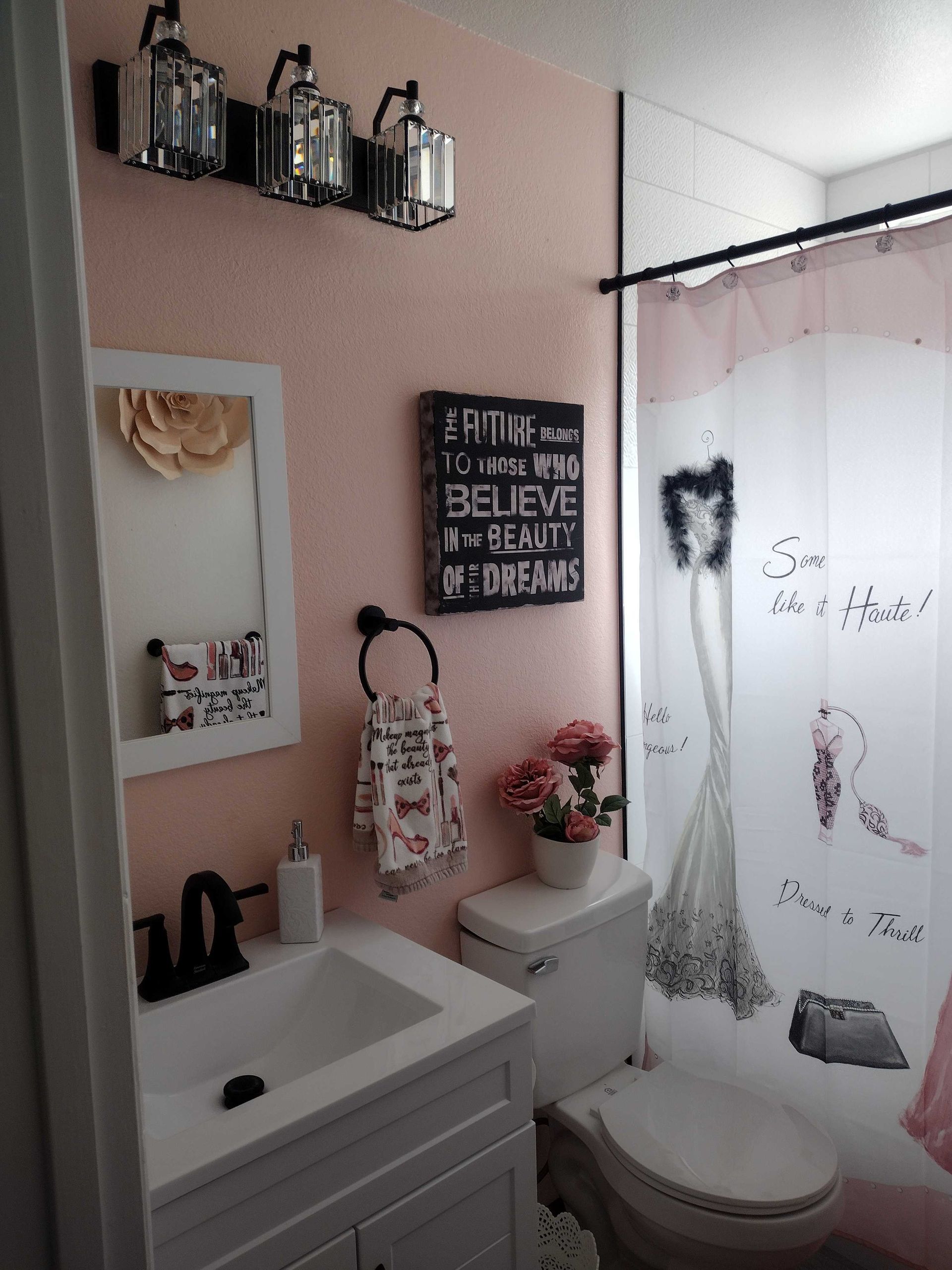 Small pink bathroom with sink, toilet, shower curtain, wall mirror, and decorative shelves.