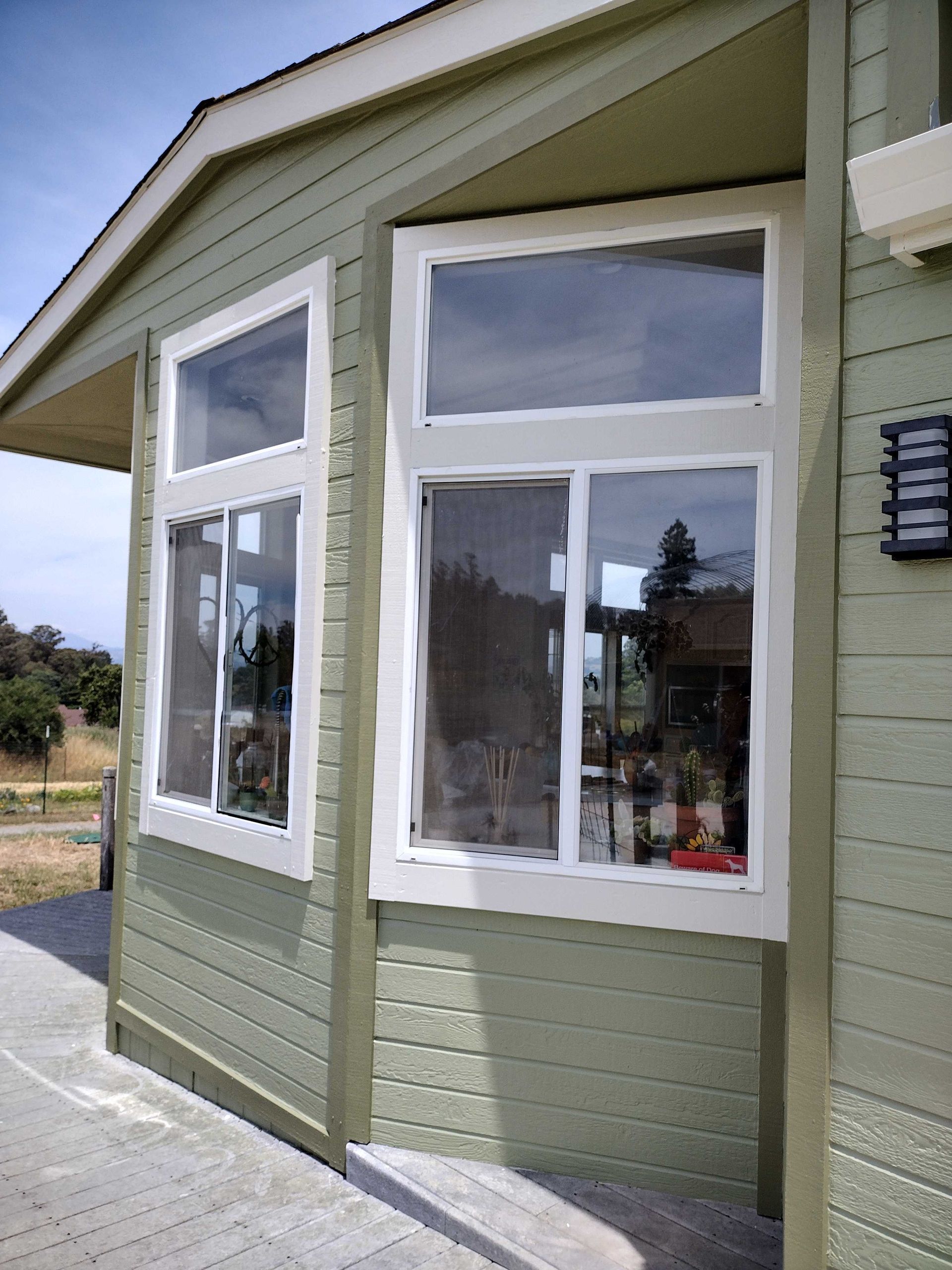 Green house exterior with large white-trimmed windows and a small paved walkway
