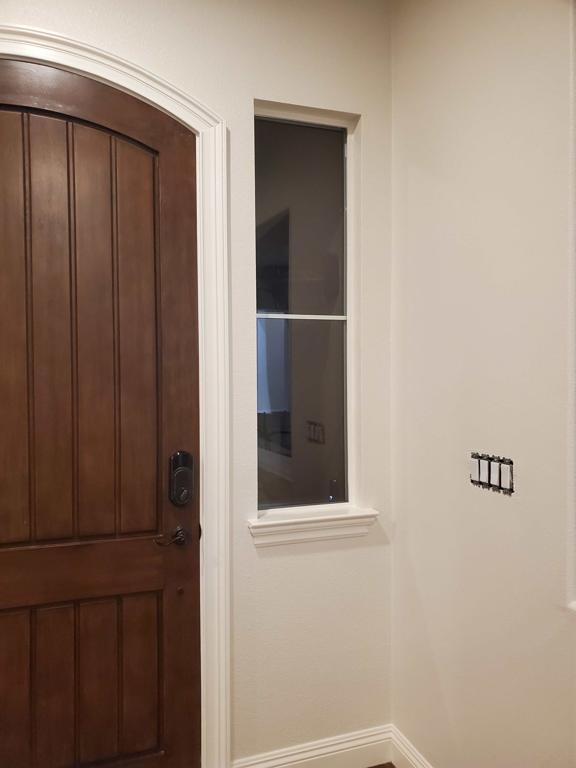 Small interior hallway with a wooden door, narrow window, and unfinished wall outlet opening