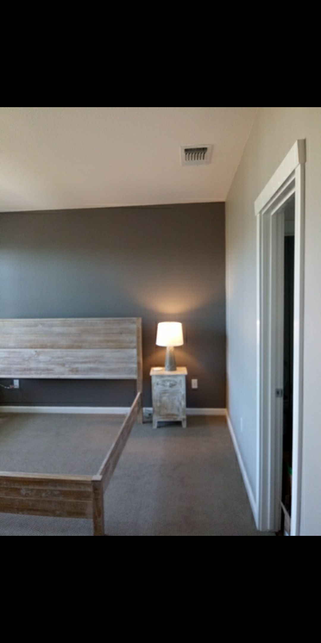 Minimal bedroom with gray walls, wooden bed frame, bedside lamp, and open closet door