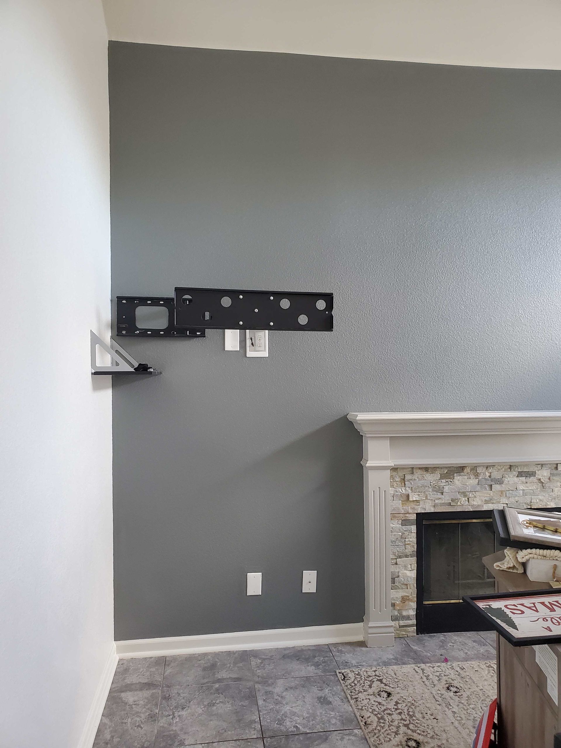 Living room wall with TV mount, gray accent paint, and a stone fireplace mantle