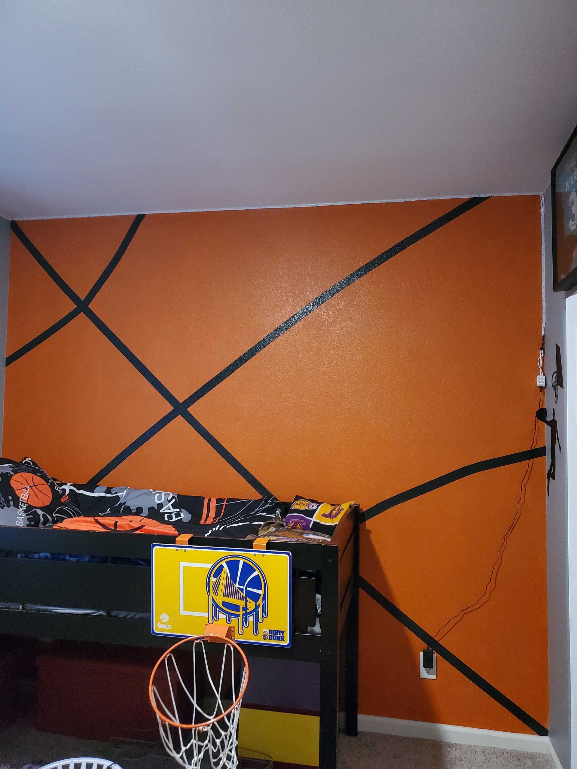 Orange wall with black diagonal lines above a basketball hoop and an arcade/game cabinet in a room