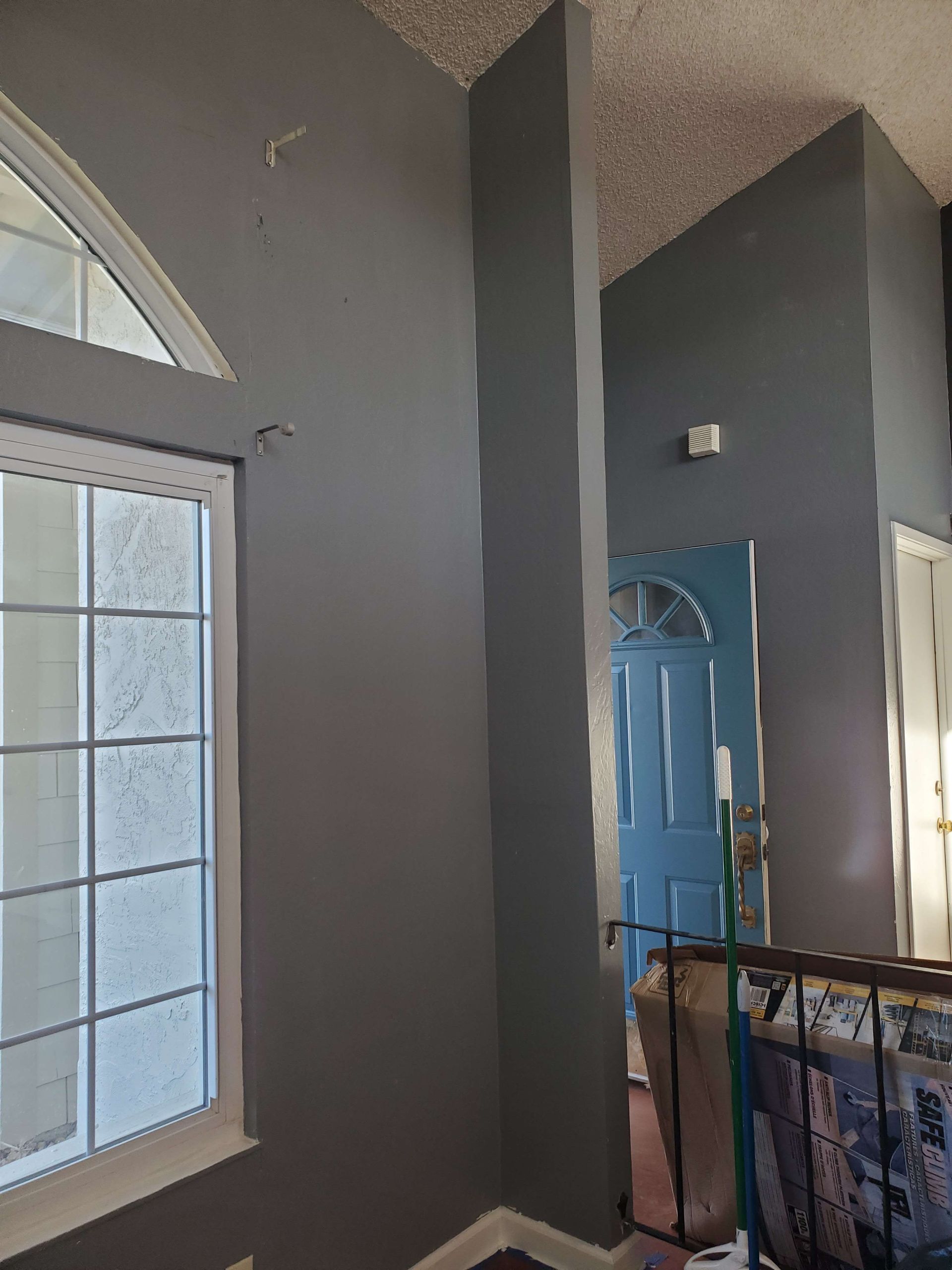 Interior stairwell with tall windows, gray walls, and a blue front door seen from an upper landing