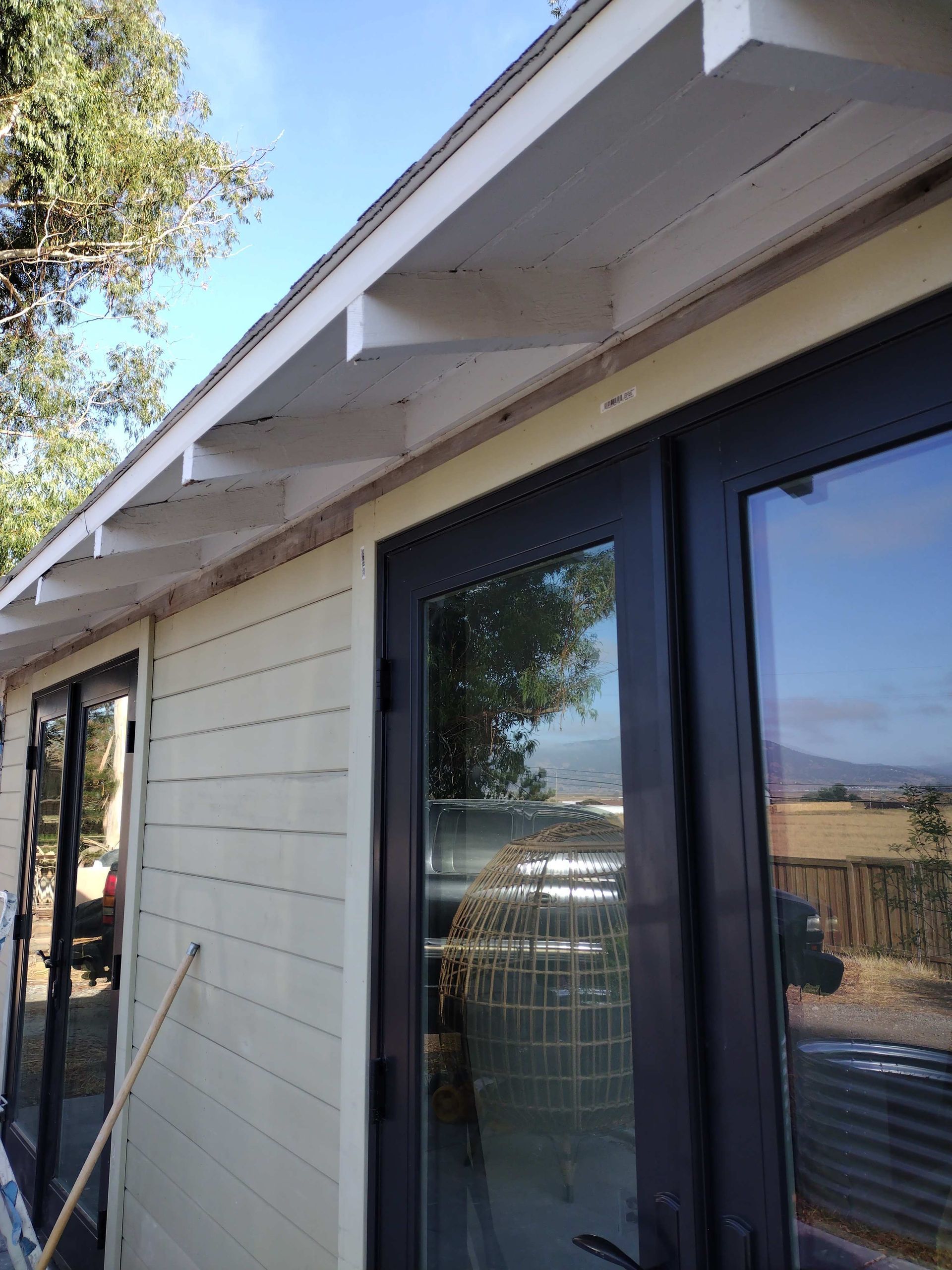 A person in a white shirt sprays gray primer onto an unfinished interior wall near a large window.