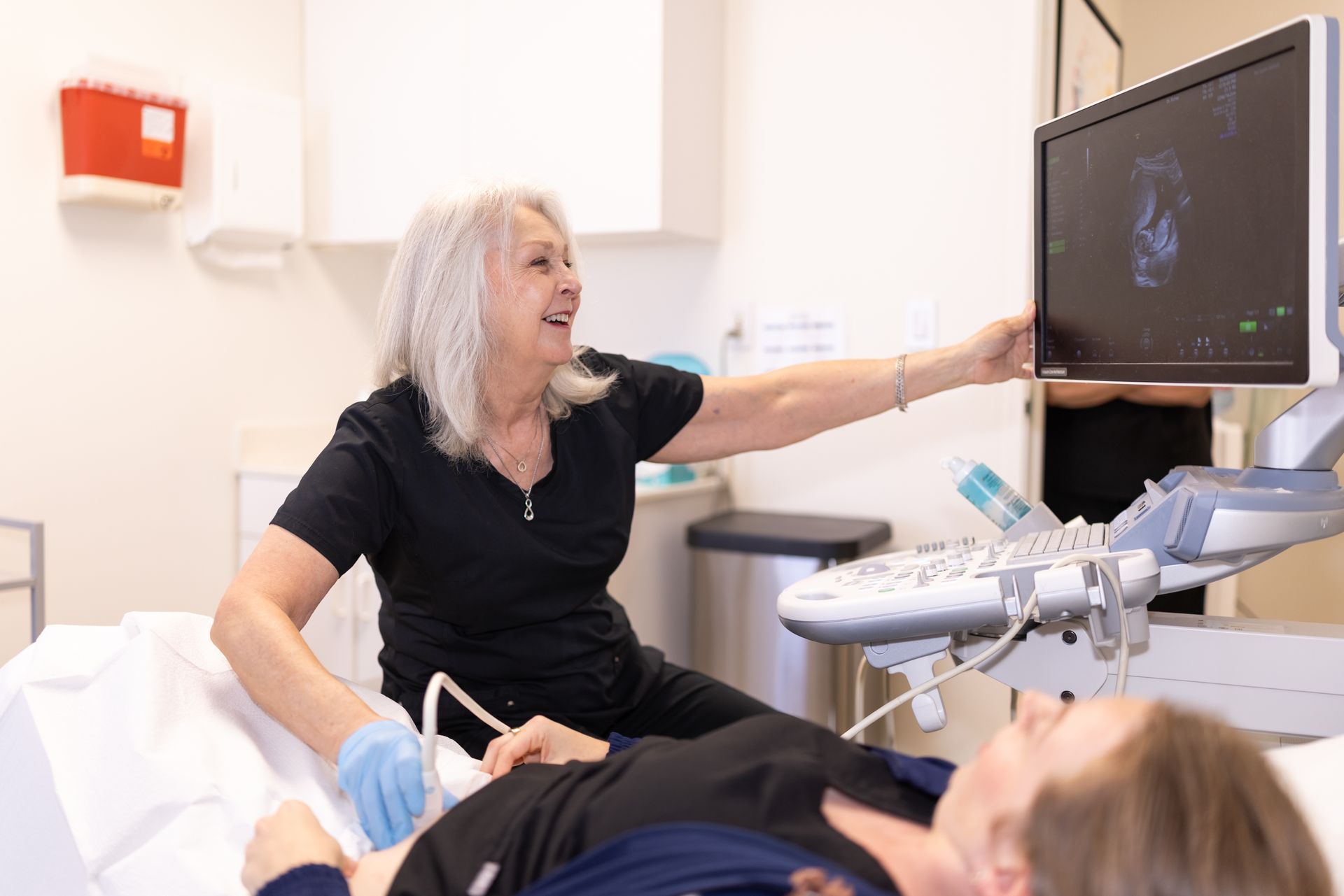 Doctor showing ultrasound on monitor in a clinic while patient lies on exam table
