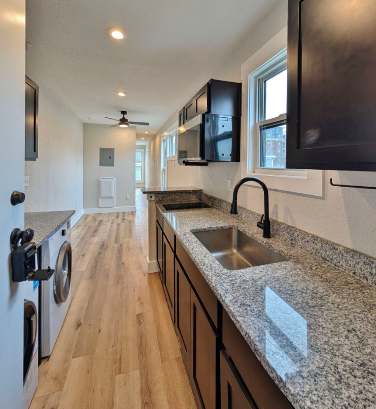 Kitchen with granite countertops, dark cabinets, stainless steel sink, and a washing machine.