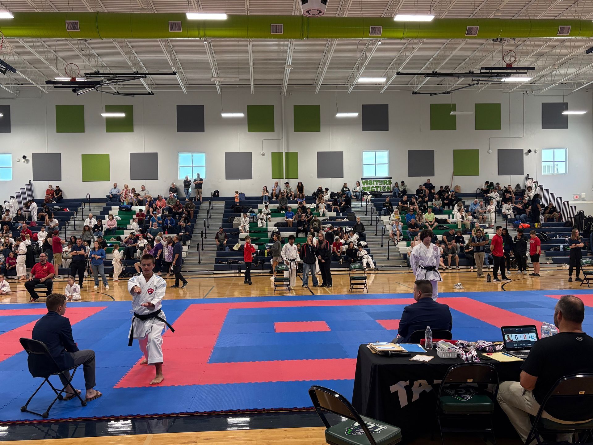 A group of kids in karate uniforms stand on a mat in front of a crowd