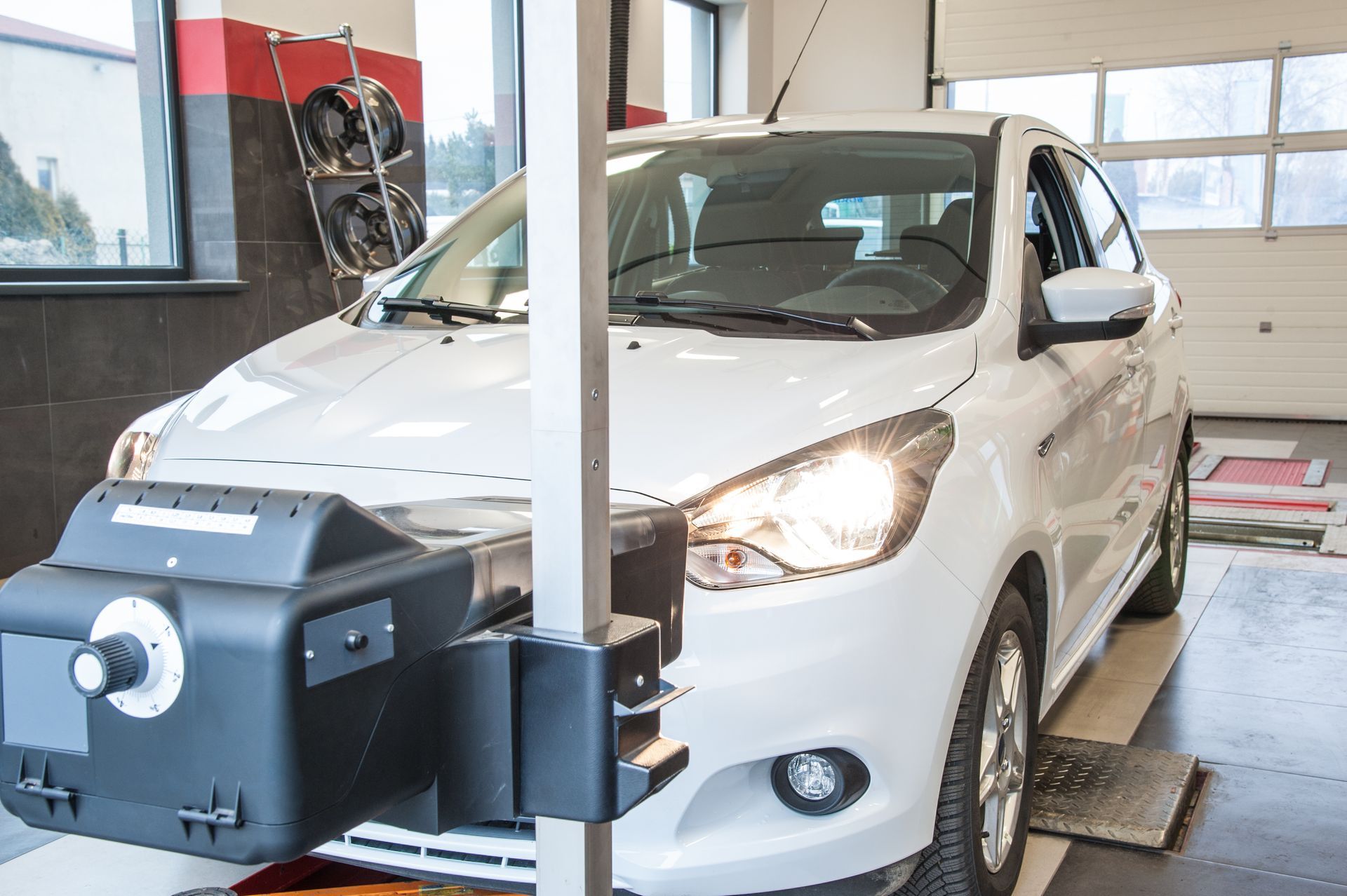 Voiture blanche sur un pont élévateur de diagnostic dans un atelier de réparation automobile, avec une machine positionnée devant elle.