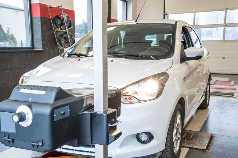 Voiture blanche sur un pont élévateur de diagnostic dans un atelier de réparation automobile, avec une machine positionnée devant elle.