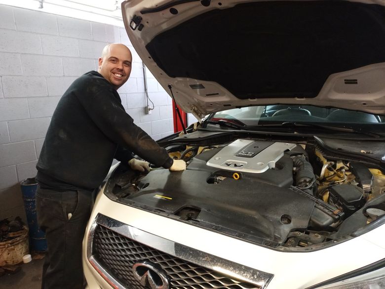Un mécanicien sourit en travaillant sous le capot d'une Hyundai blanche dans un garage.