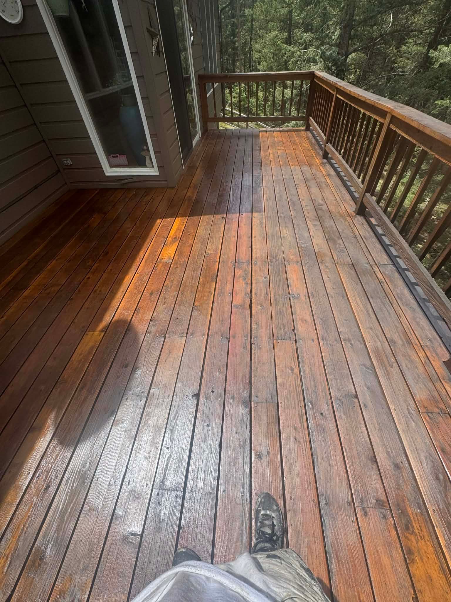 Wet wooden deck with railings and sunlight, viewed from standing position