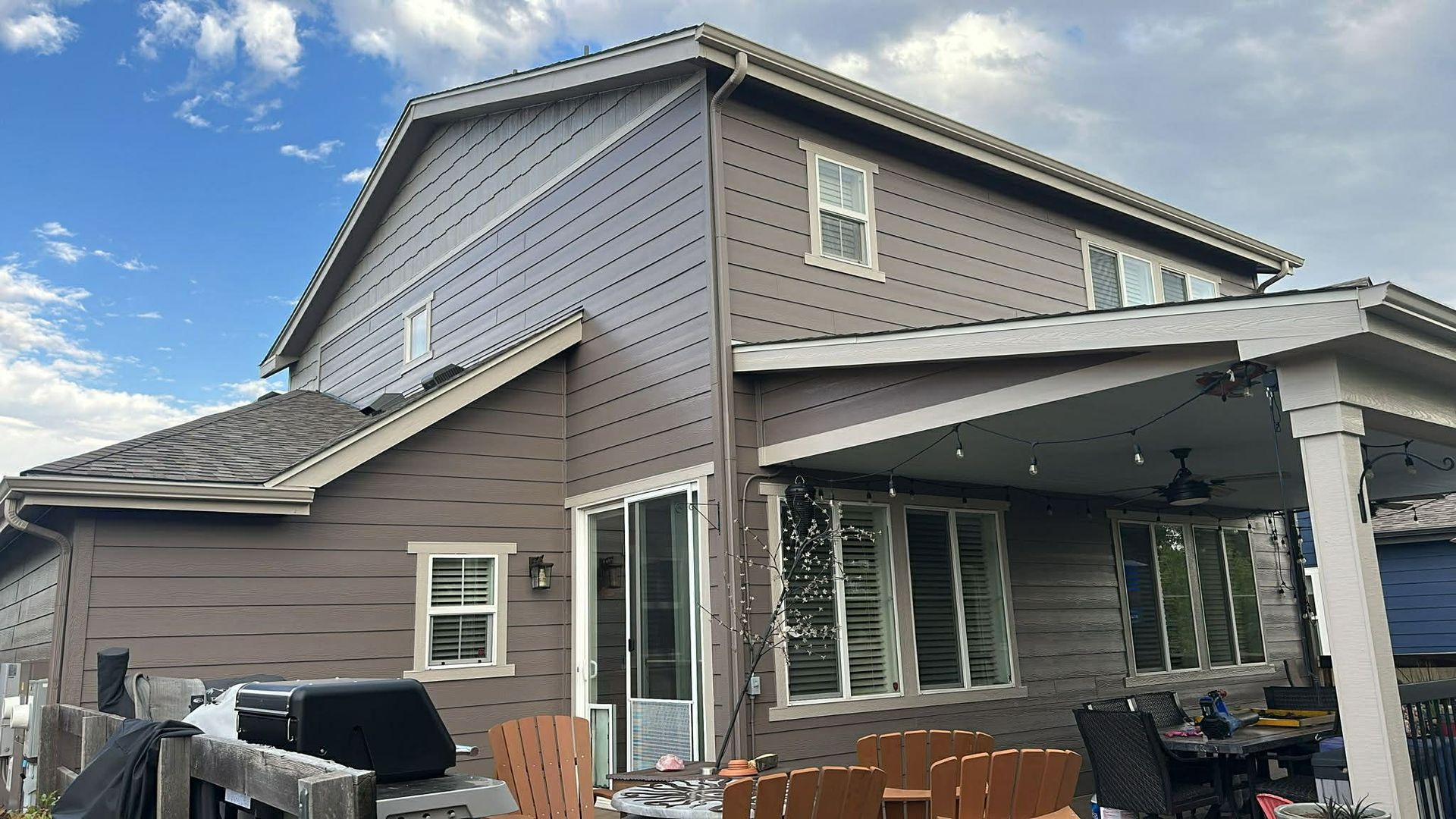 Gray house with covered patio, white trim, and outdoor furniture under a cloudy sky