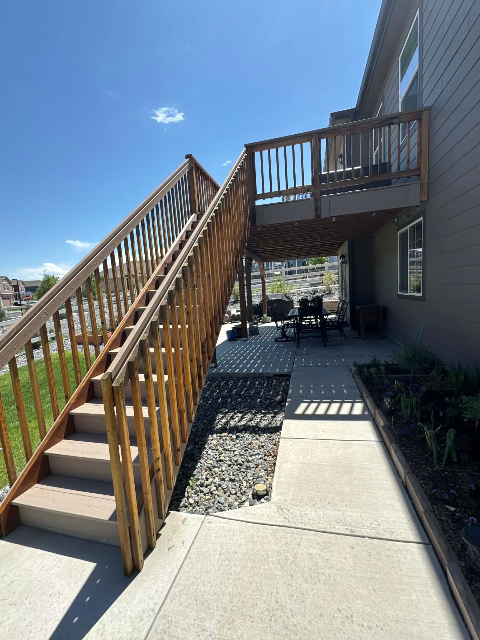 Outdoor stairs leading to a wooden balcony and patio outside a house, with sunny blue sky above