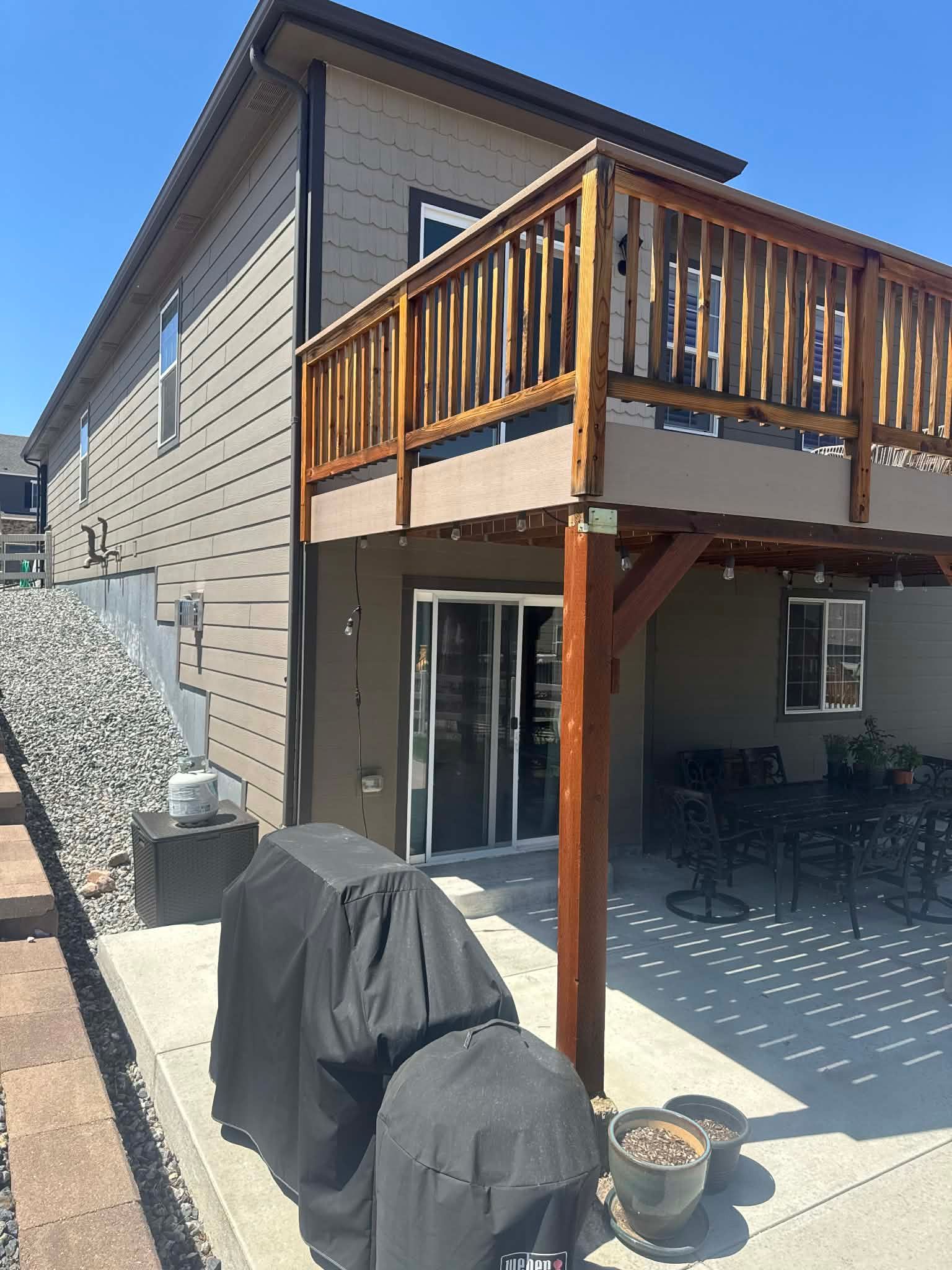 Backyard patio under a wooden deck with sliding glass doors and a covered grill in the foreground