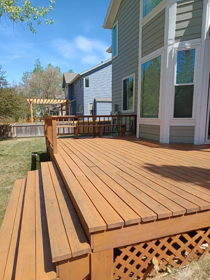 Wooden backyard deck beside a light gray house, with railings and lattice skirting under a sunny blue sky