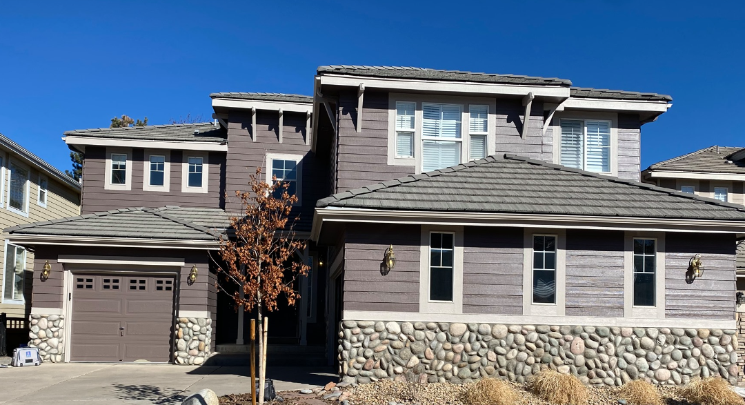 Modern two-story suburban house with stone and wood exterior, garage, and snow-covered ground