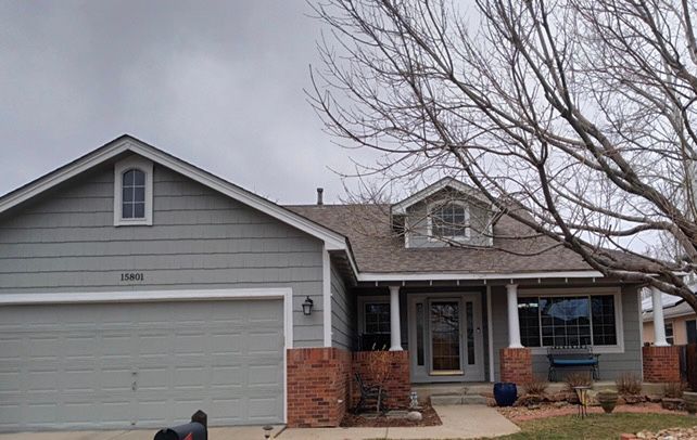 Gray suburban house with a two-car garage, front porch, and bare trees in front
