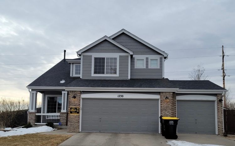 Two-story gray house with a double garage and snow on the ground at dusk
