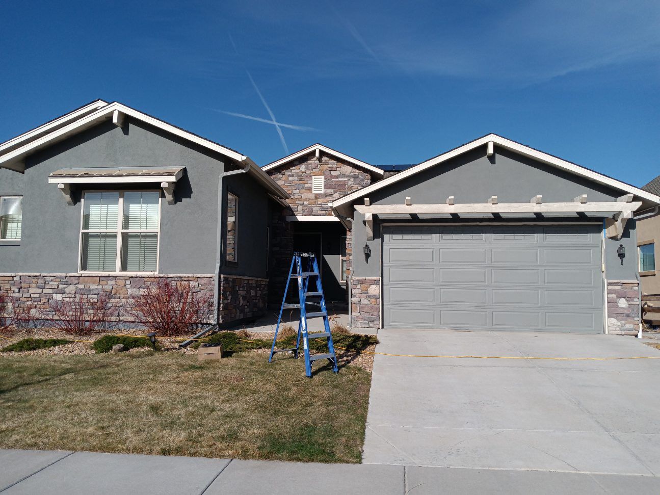 Single-story suburban house with a blue ladder on the front lawn and a two-car garage.