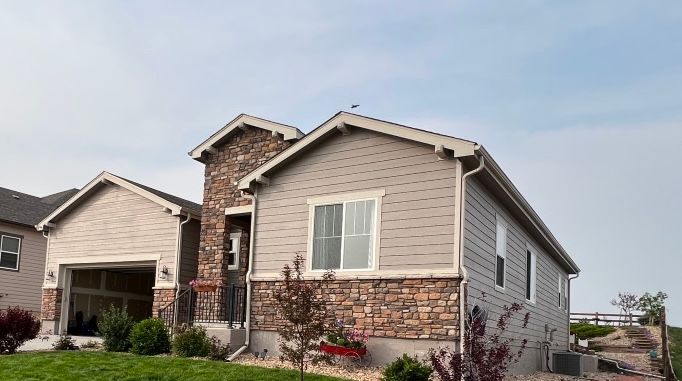 Suburban house with beige siding, stone accents, and a two-car garage under a partly cloudy sky