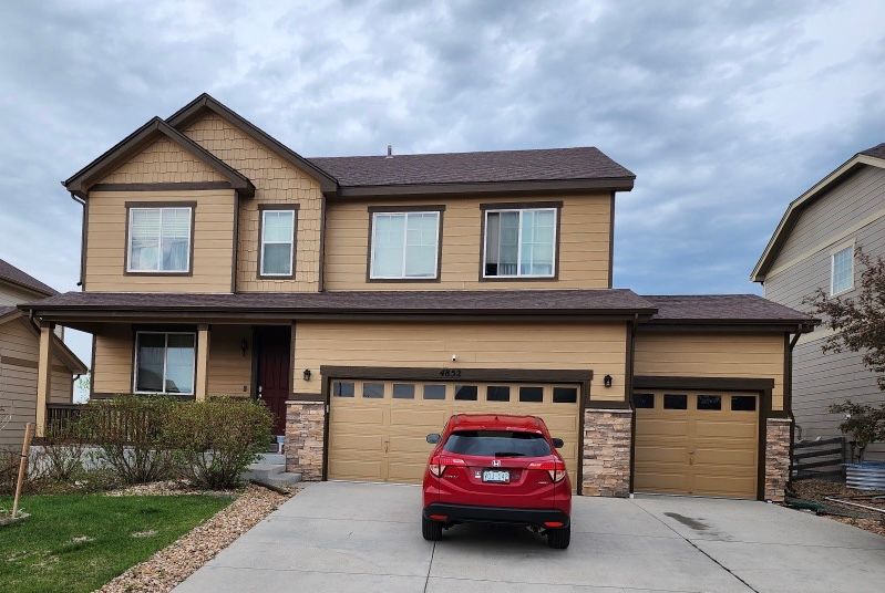 Suburban two-story house with beige siding, a red SUV parked in the driveway, and cloudy sky overhead