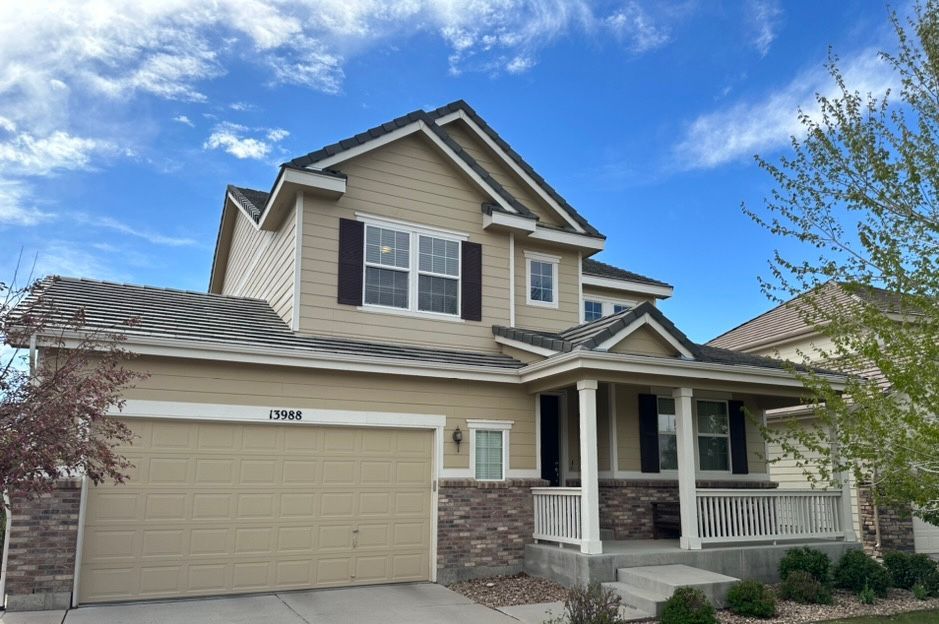 Two-story beige suburban house with a two-car garage and covered front porch under a blue sky