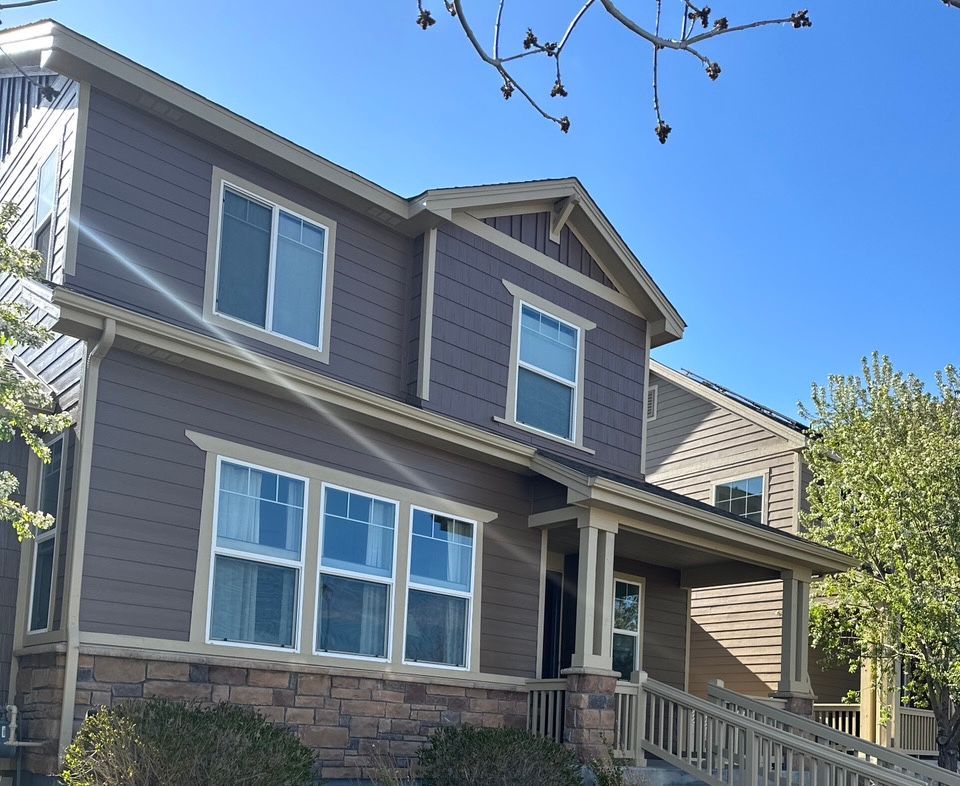 Two-story gray house with white trim, stone base, and a front porch under a clear blue sky