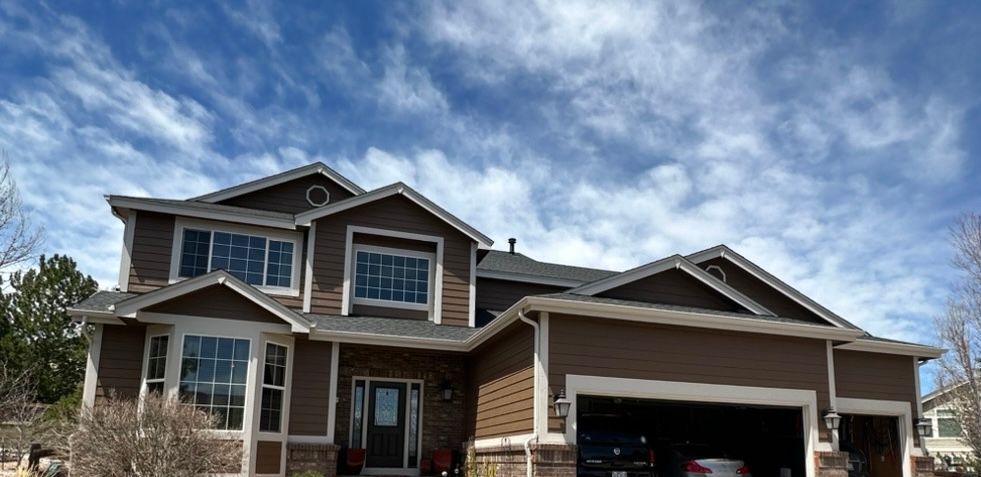 Two-story suburban house with a stone facade, front porch, and three-car garage under a cloudy sky