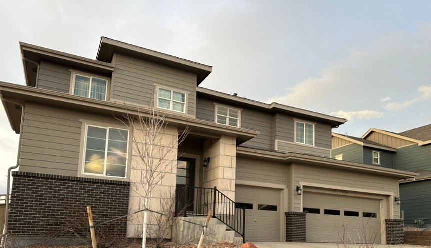 Modern two-story suburban house with gray siding, large windows, and a three-car garage at dusk