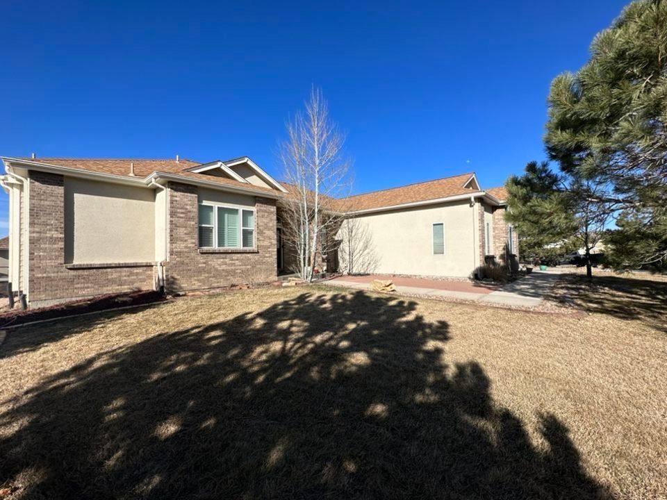 Suburban house with beige siding and stone facade under a clear blue sky, front yard in winter light