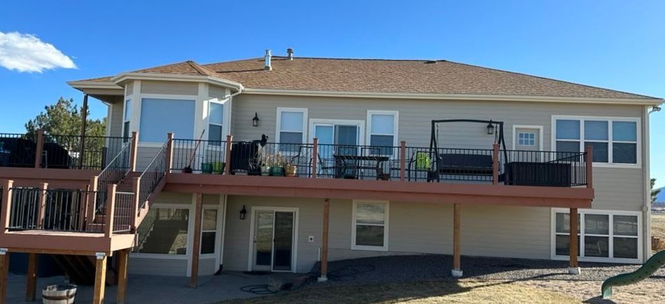 Two-story beige house with a large wooden deck and patio furniture under a clear blue sky