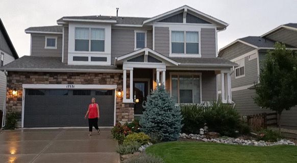 Two-story suburban house with a garage, stone accents, and a person in a red jacket on the driveway
