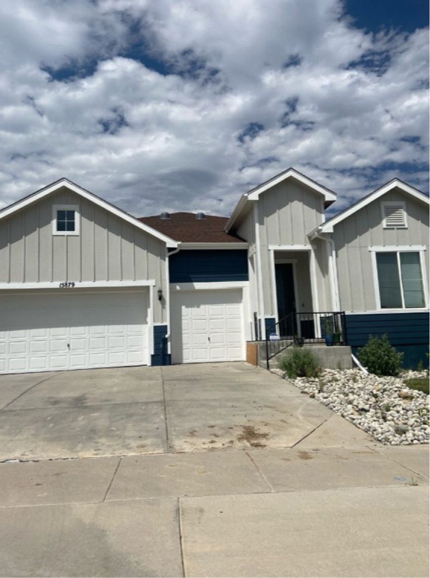 Suburban house with a double garage, gray siding, and a concrete driveway under a cloudy sky