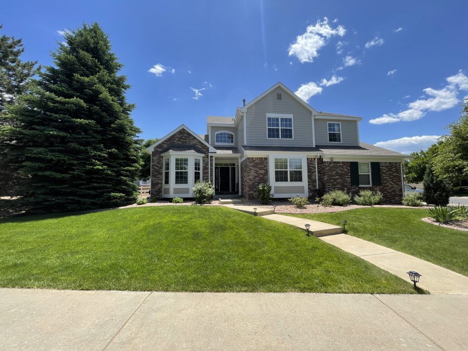 Suburban two-story house with a manicured lawn, stone facade, and clear blue sky