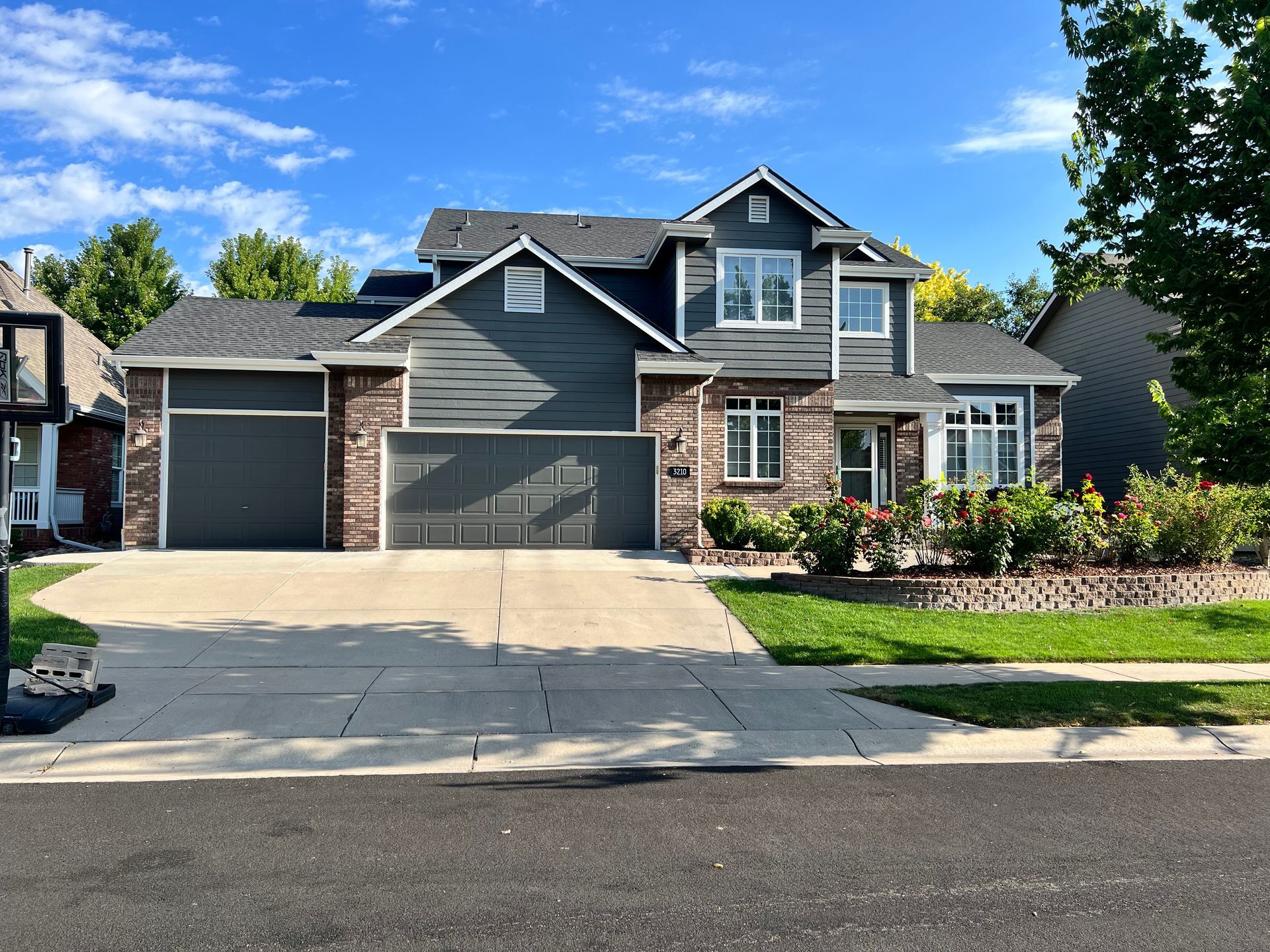 Suburban two-story gray house with a driveway, garage, front garden, and blue sky.