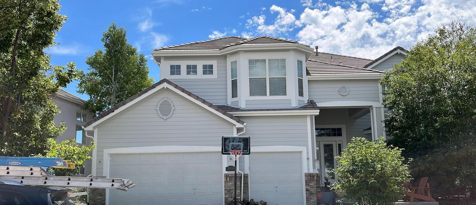 White two-story suburban house with a garage, front porch, and trees under a blue sky