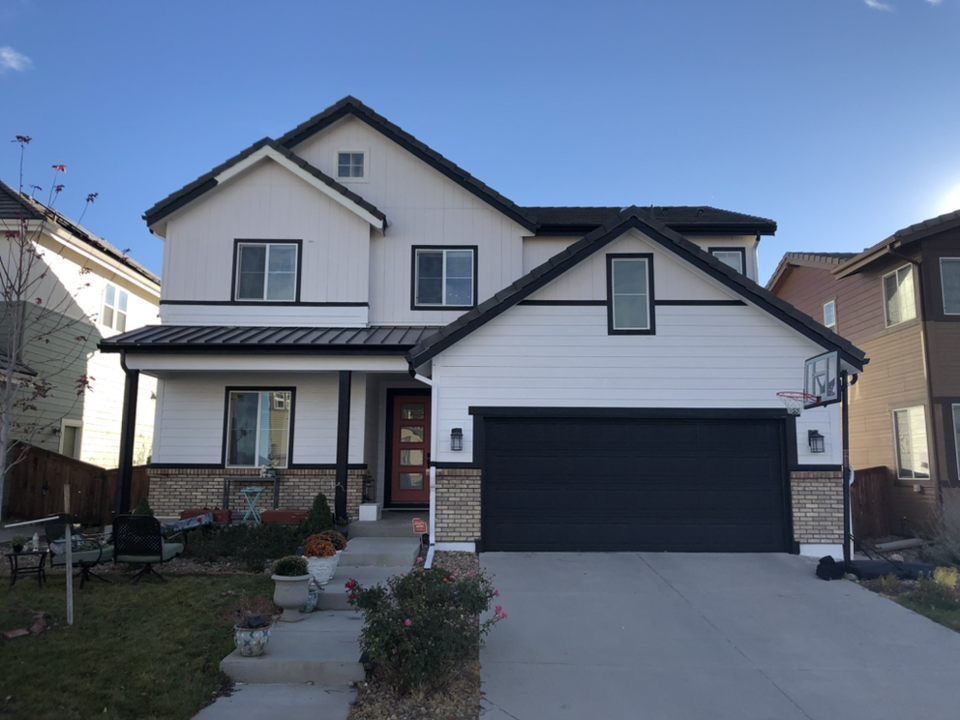 Two-story beige house with black roof and garage, front walkway and small lawn under clear sky