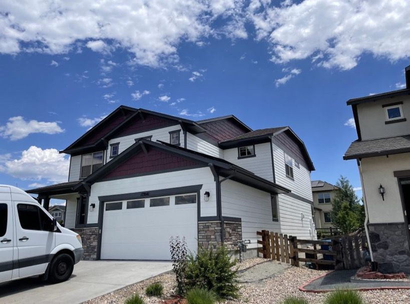 Modern two-story suburban house with a white garage, stone accents, and a blue sky overhead