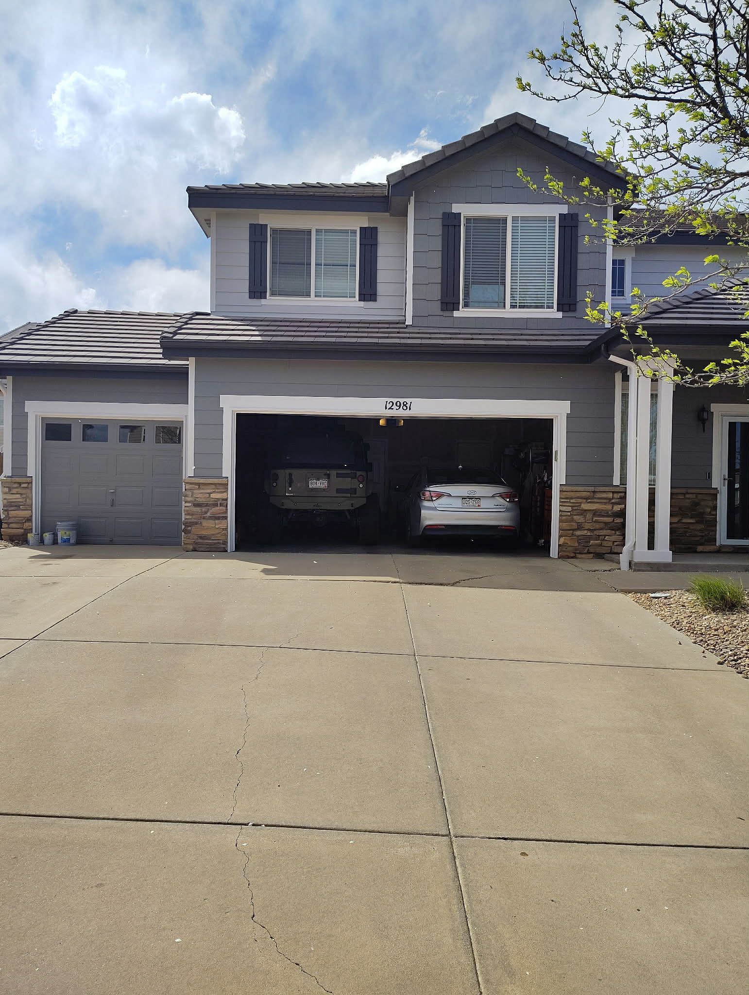 Suburban two-story house with a double garage and two cars in the driveway under a partly cloudy sky
