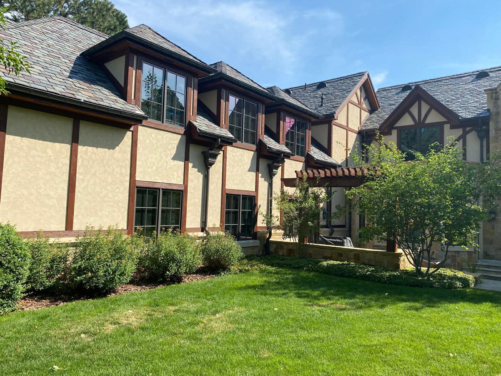 Tudor-style house with cream walls, dark wood trim, and a green front lawn under sunny skies