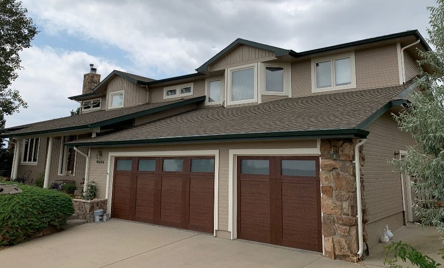 Suburban two-story house with brown garage doors and a beige stone exterior under an overcast sky