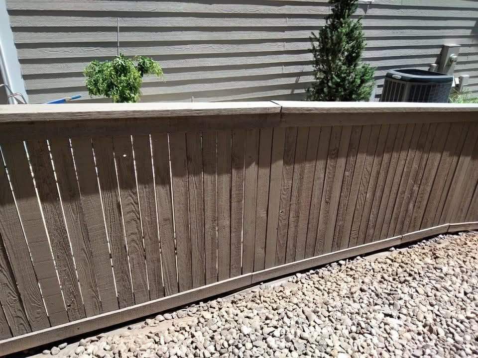 Brown wooden fence with slats beside a gravel yard and beige house siding